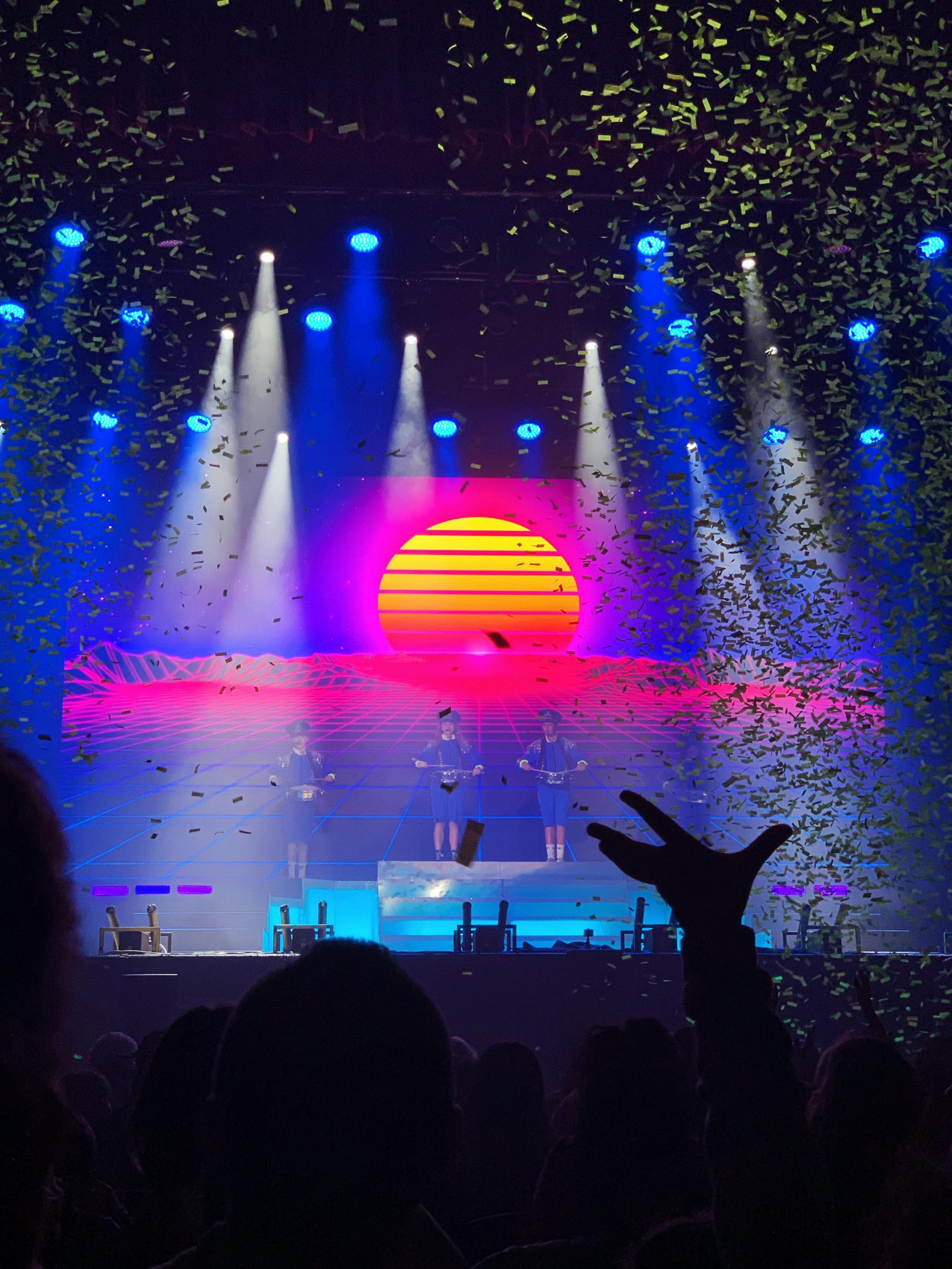 Dynamic concert scene with performers under colorful lights and confetti, vibrant atmosphere.